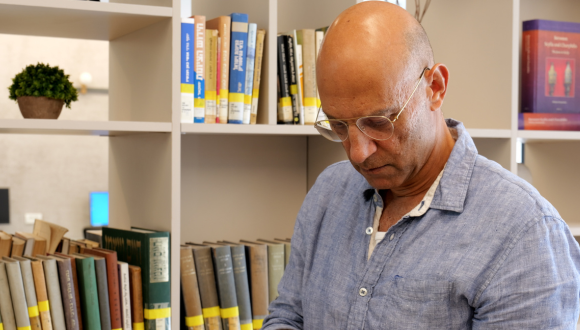 Prof Youval Rotman in the Mehlman Library at TAU, standing in front of bookshelves